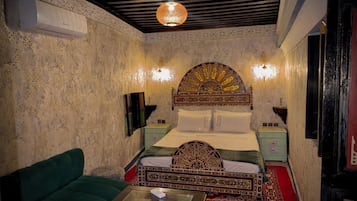 Una habitación con cama, sofá verde, cabecero decorativo, lámparas de pared y una lámpara en el techo.