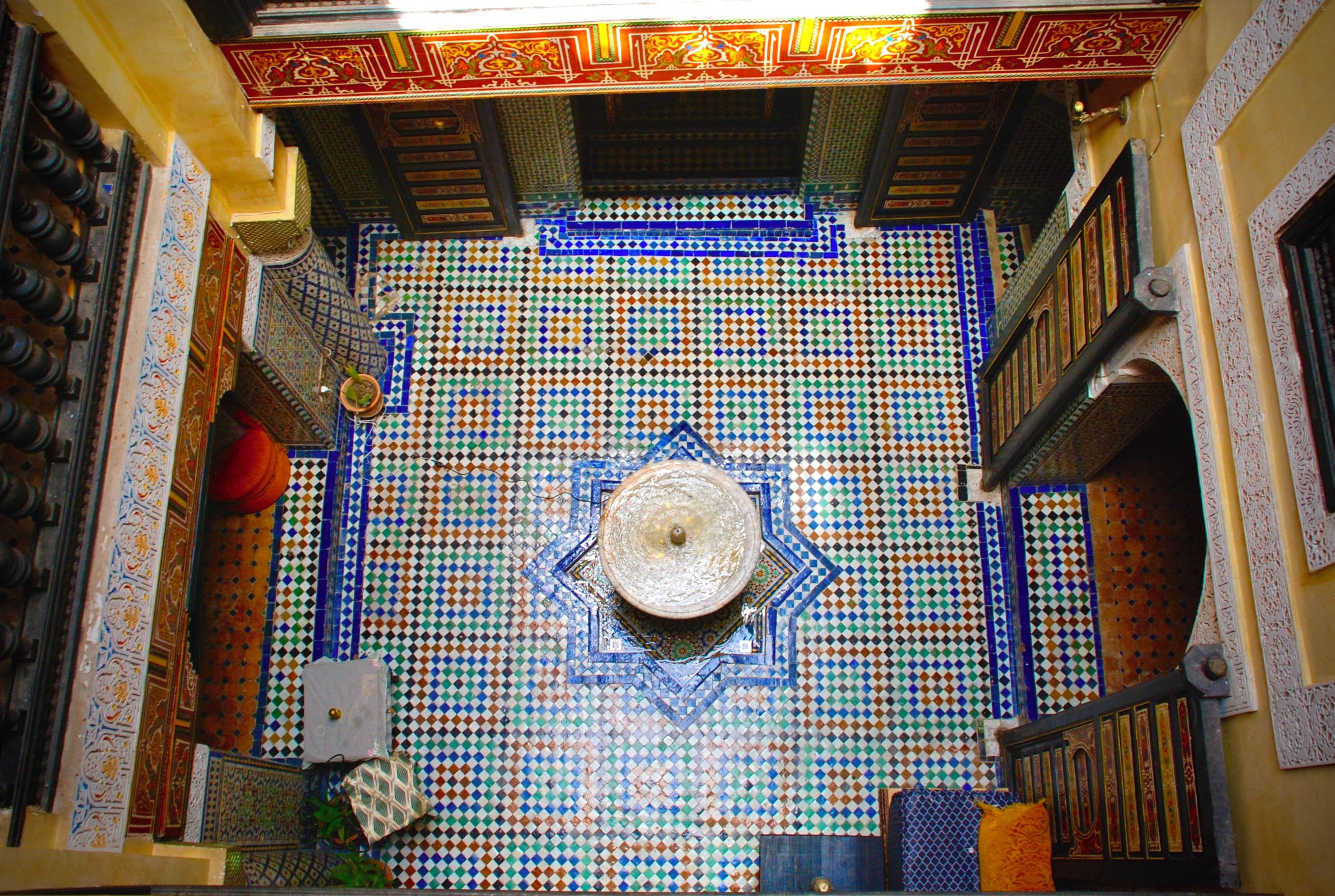 A room with a patterned tile wall, a central decorative element, and a door with intricate design.