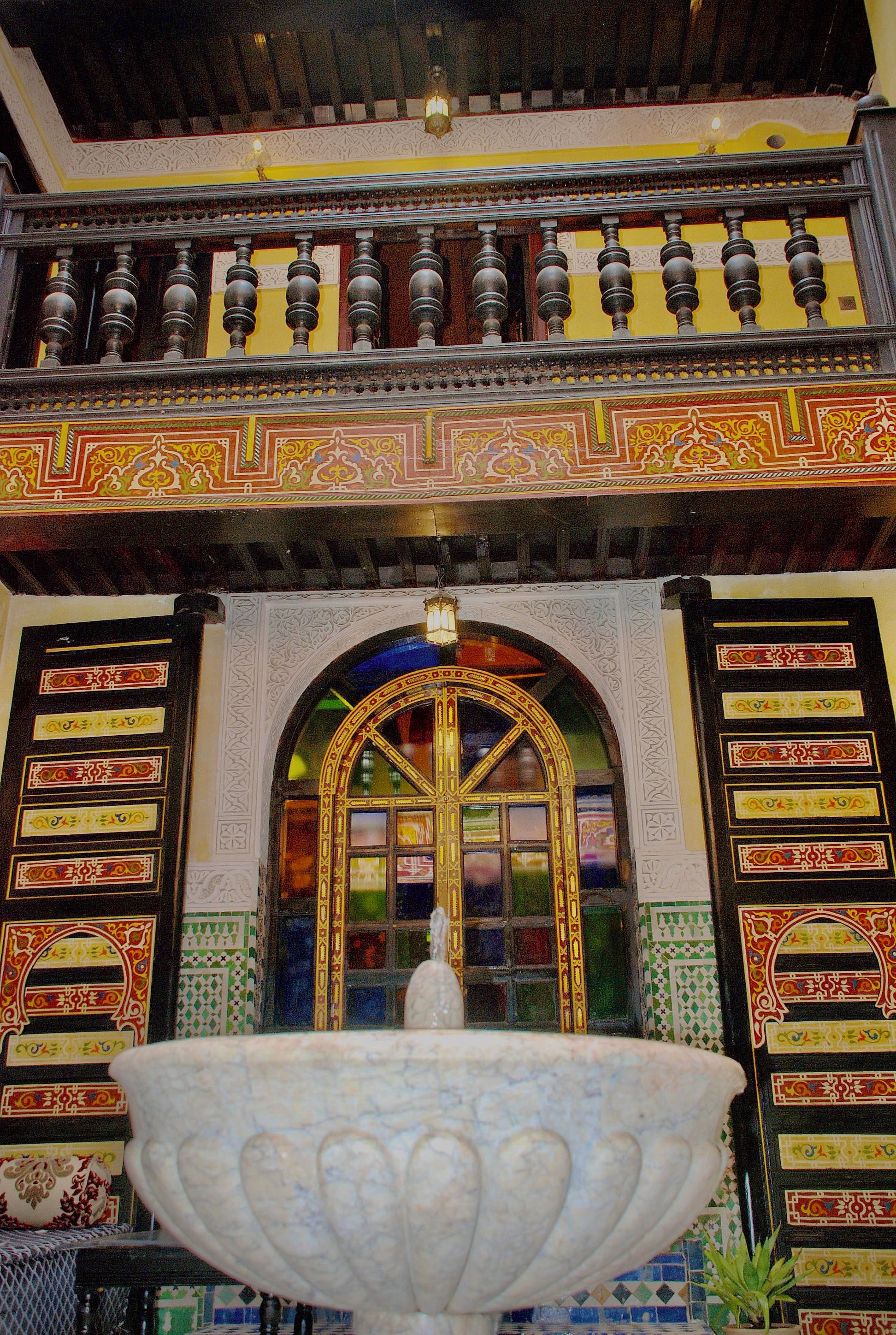 An ornate fountain with intricate designs, a detailed ceiling with decorative patterns, and a wall with colorful geometric tile work.