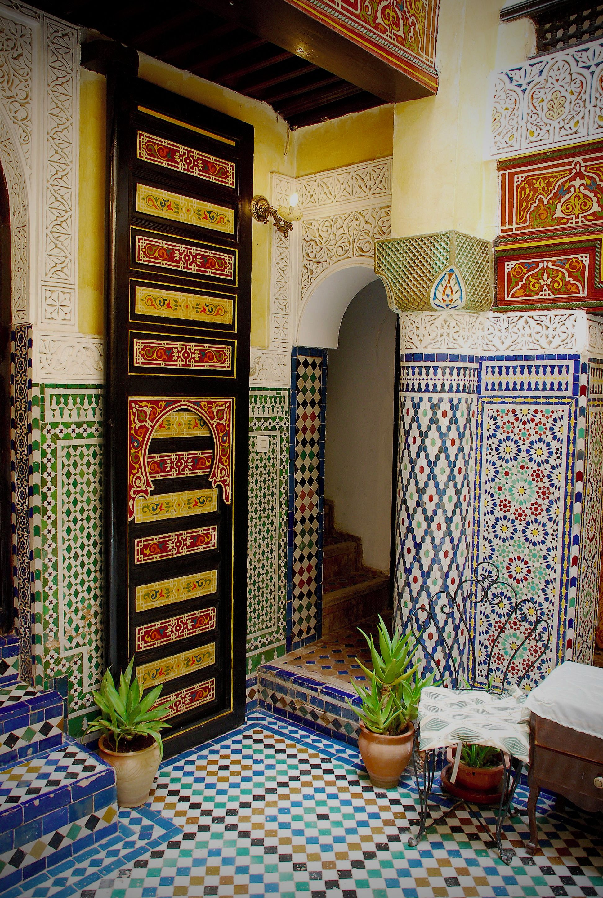 Ein traditionelles marokkanisches Interieur mit gefliestem Eingang, einer Holztür mit aufwendigen Verzierungen und Blumentöpfen.