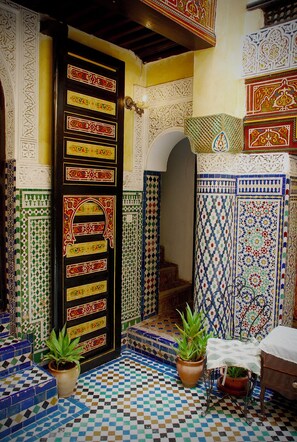 A traditional Moroccan interior with a tiled entrance, a wooden door with intricate designs, and potted plants. - Palais Doha & SPA (Fes)