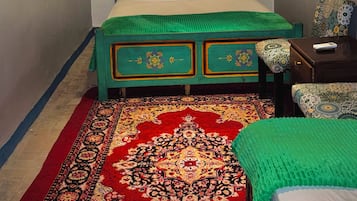 Una habitación con una cama, una mesita de noche, una lámpara, un tapete estampado y un cabecero decorativo.