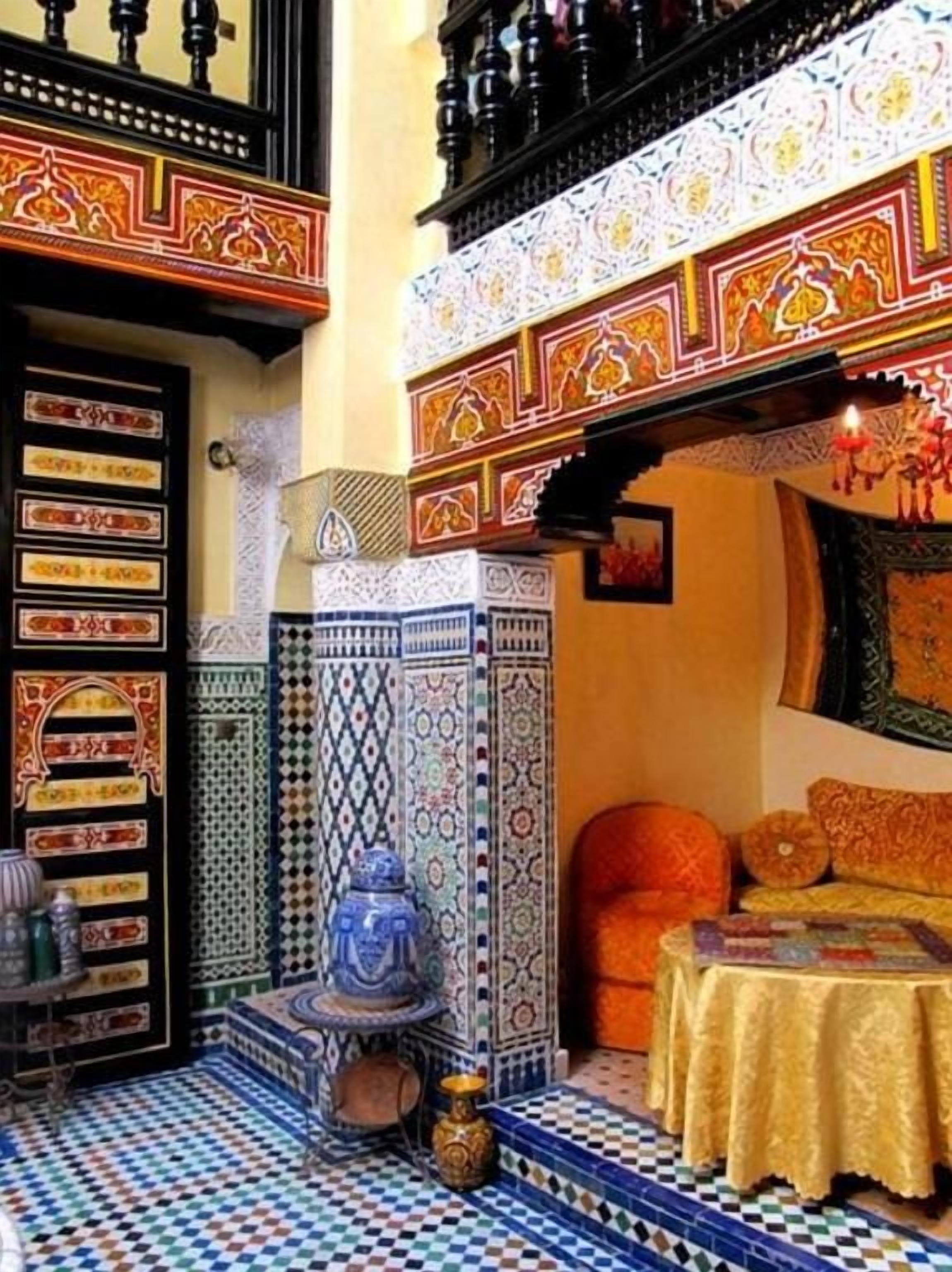 A traditional Moroccan interior with a tiled courtyard, a blue ceramic pot, and a patterned wall.