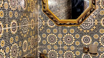 Un baño con pared decorada con azulejos, un lavamanos con lavabo a rayas negras y blancas, y un espejo con marco dorado.