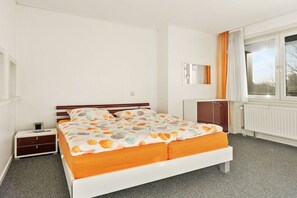 Ein Schlafzimmer mit einem Bett, einem Nachttisch, einer Kommode, einem Fenster mit Vorhängen und einer Heizung.