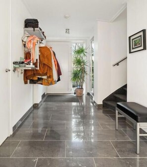 Un couloir avec un banc, un porte-manteau sur lequel sont suspendus des vêtements et une plante en pot.