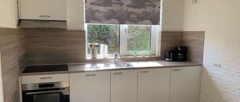 A modern kitchen with white cabinetry, a built-in oven, a stainless steel sink, and a window with a camouflage blind.