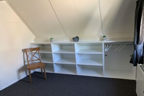 Une pièce avec un plafond en pente, une chaise en bois, des étagères blanches et une petite plante en pot.