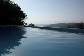 A clear view of a swimming pool with calm water, surrounded by trees and distant hills. - Holiday home in Colognac with swimming pool (Colognac)