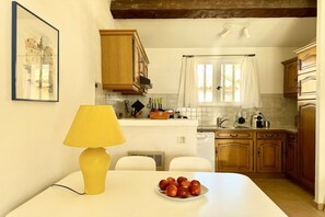Une cuisine avec des meubles de rangement en bois, un plan de travail blanc et une fenêtre avec des rideaux.