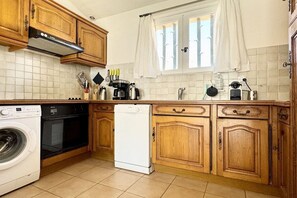 A kitchen with wooden cabinets, a dishwasher, a washing machine, and a window with curtains. - Holiday apartment with 1 bedroom (Cavalaire sur Mer)
