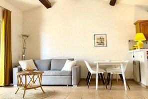 A living room with a grey sofa, a small round table with fruits, white chairs, and a yellow lamp. - Holiday apartment with 1 bedroom (Cavalaire sur Mer)