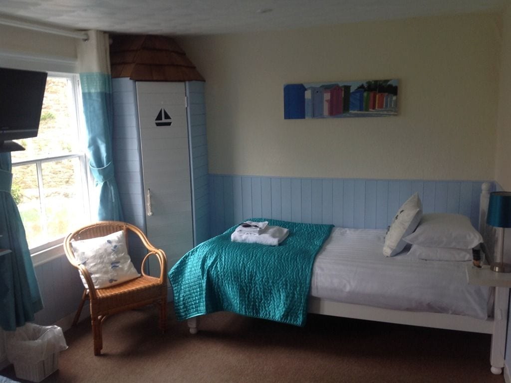 A bedroom with a bed, a chair, a window with curtains, and a wall-mounted television.