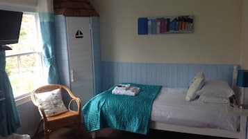 A bedroom with a bed, a chair, a window with curtains, and a wall-mounted television.