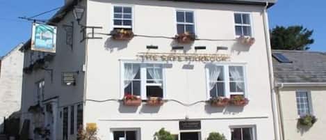 A white building with a sign reading 'The Sea Harbours.' It has multiple windows, outdoor seating, and potted plants.
