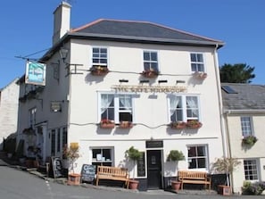 A white building with a sign reading 'The Sea Harbours.' It has multiple windows, outdoor seating, and potted plants.