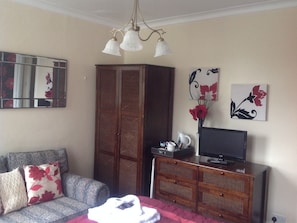 A room with a sofa, a television on a wooden cabinet, a mirror, and artwork on the wall.