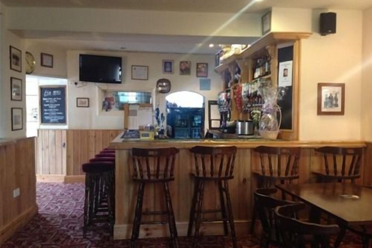 A bar area with wooden bar stools, a television mounted on the wall, and a menu board.