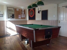 Una mesa de billar en una habitación con suelo de madera, un dardo y una puerta.