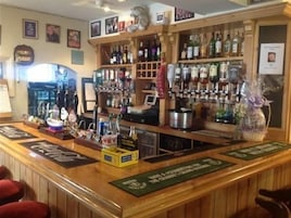 Zona de bar con estantes de botellas, una caja registradora y un atril para el menú.