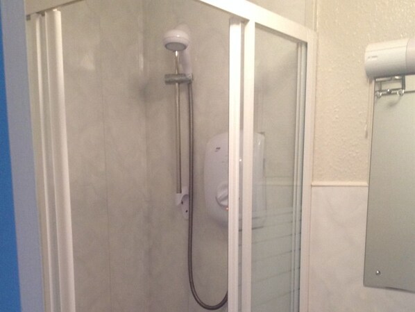 A shower enclosure with a glass door, a handheld showerhead, and a wall-mounted control panel.