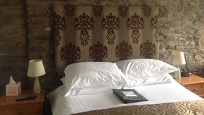 A bed with white linens, a decorative headboard, and a nightstand with a lamp and remote control.