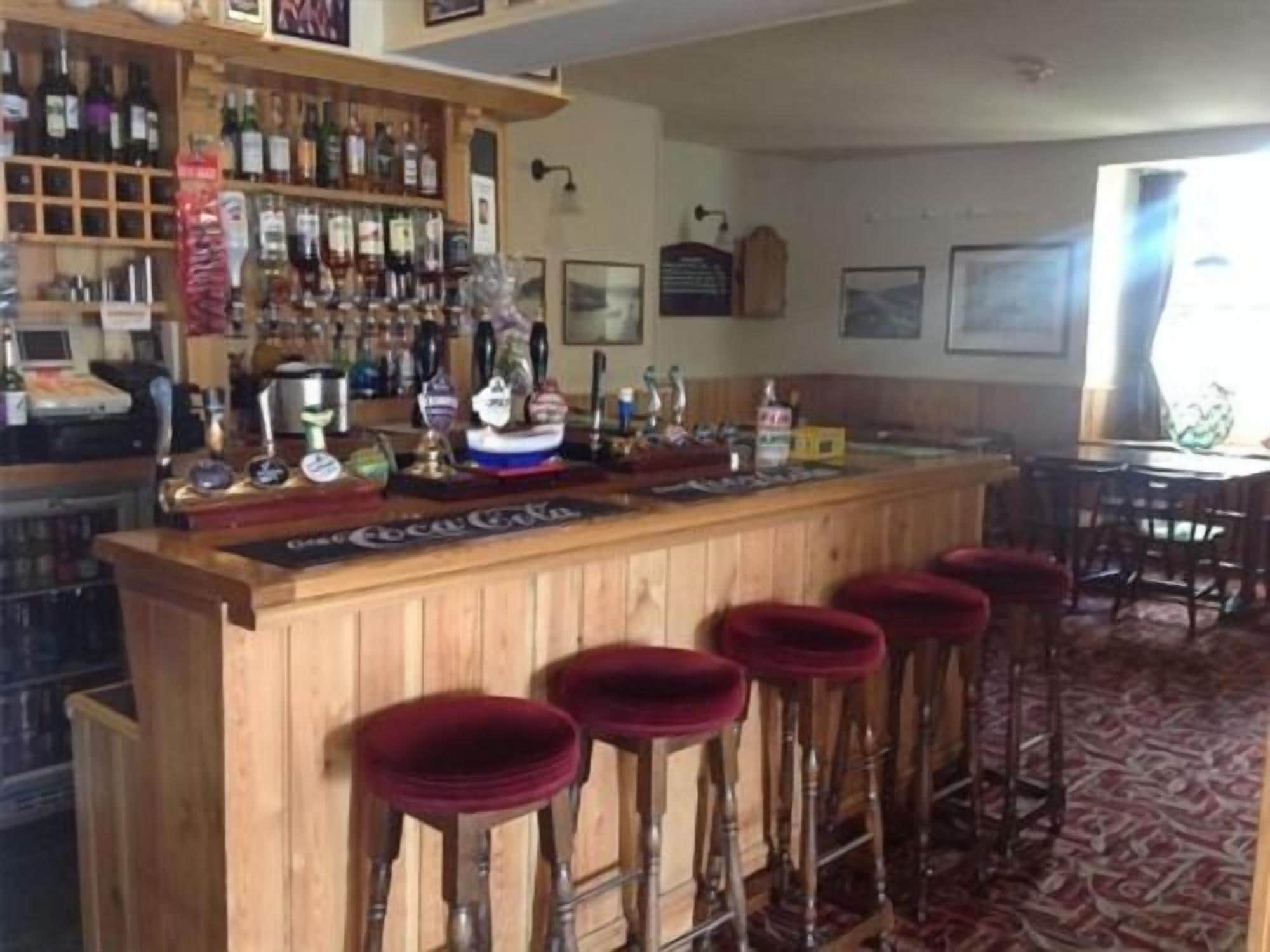 A bar area with wooden stools, a counter with various bottles, and a red carpeted floor.