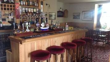 A bar area with wooden stools, a counter with various bottles, and a red carpeted floor.