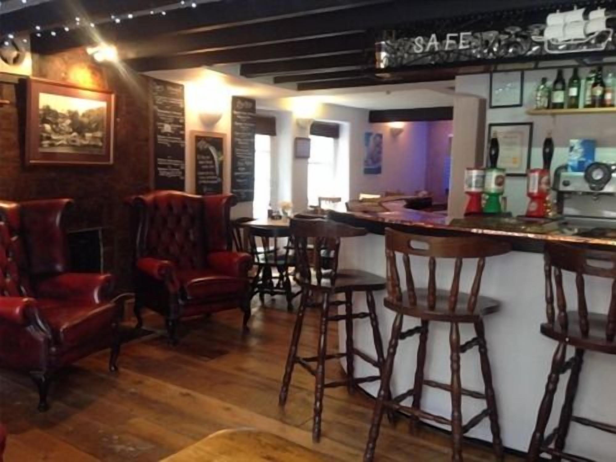 Zona de bar con taburetes de madera, una barra con botellas y un panel con la carta.