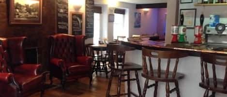 A bar area with wooden bar stools, a counter with bottles, and a menu board.