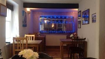 A dining area with wooden tables and chairs, a vase with flowers, and a wall with framed pictures.