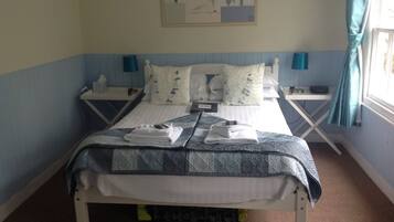 A neatly made bed with a blue and white patterned bedspread, two bedside tables with lamps, and a painting on the wall.