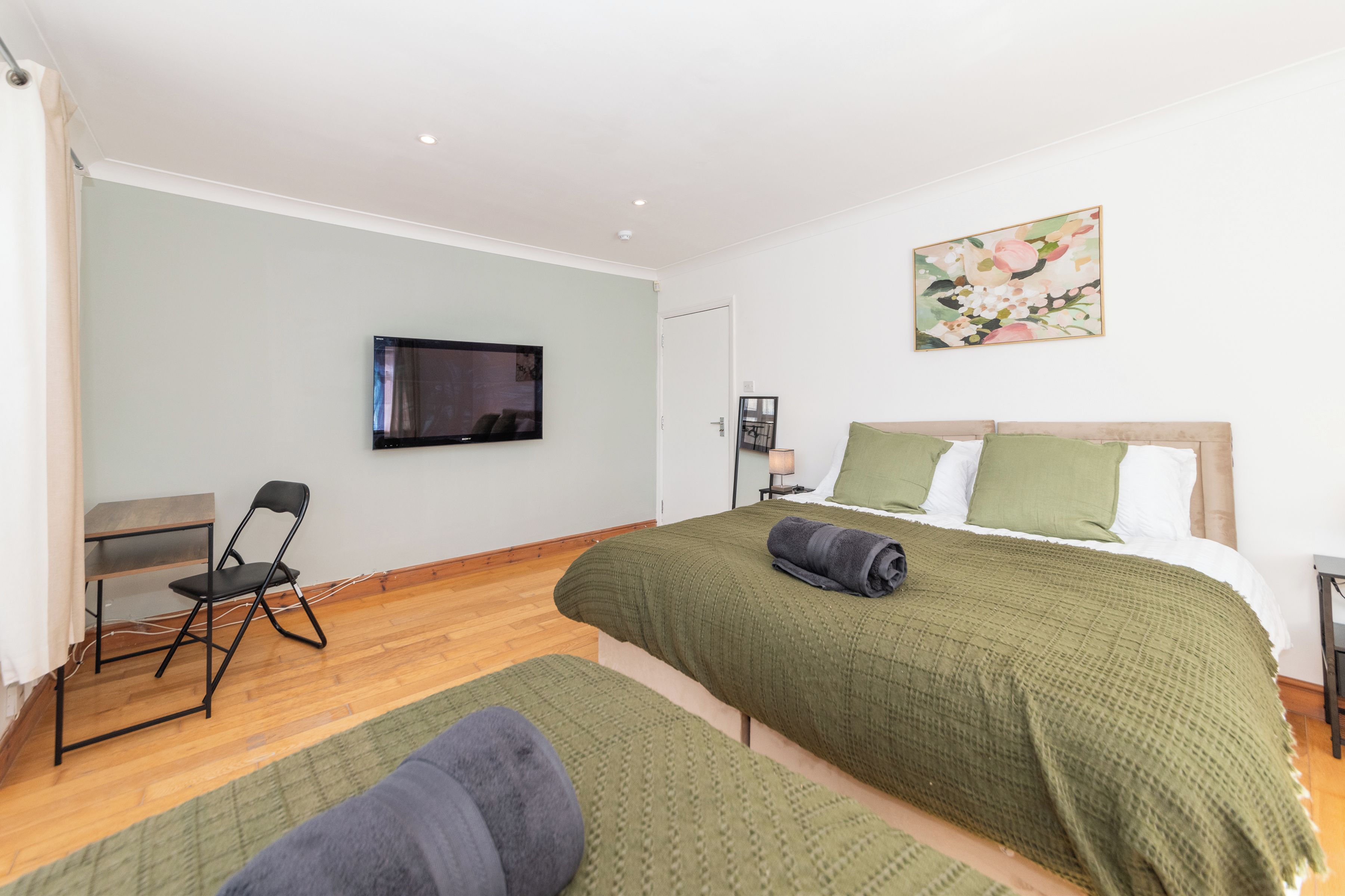 A bedroom with two beds, a desk, a chair, a television, and a painting on the wall.