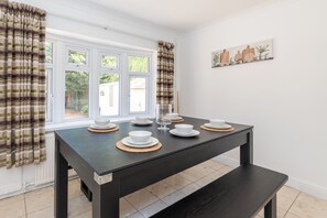 A dining area with a table set for four, a bench, and a window with curtains. - Spacious 5BR Home, Contractor Stay, Free Parking (Wraysbury)