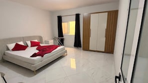 A bedroom with a bed, a wardrobe, a window with curtains, and a tiled floor. - AC • King Bed • Full Kitchen • Fast Wi-Fi (Praia)