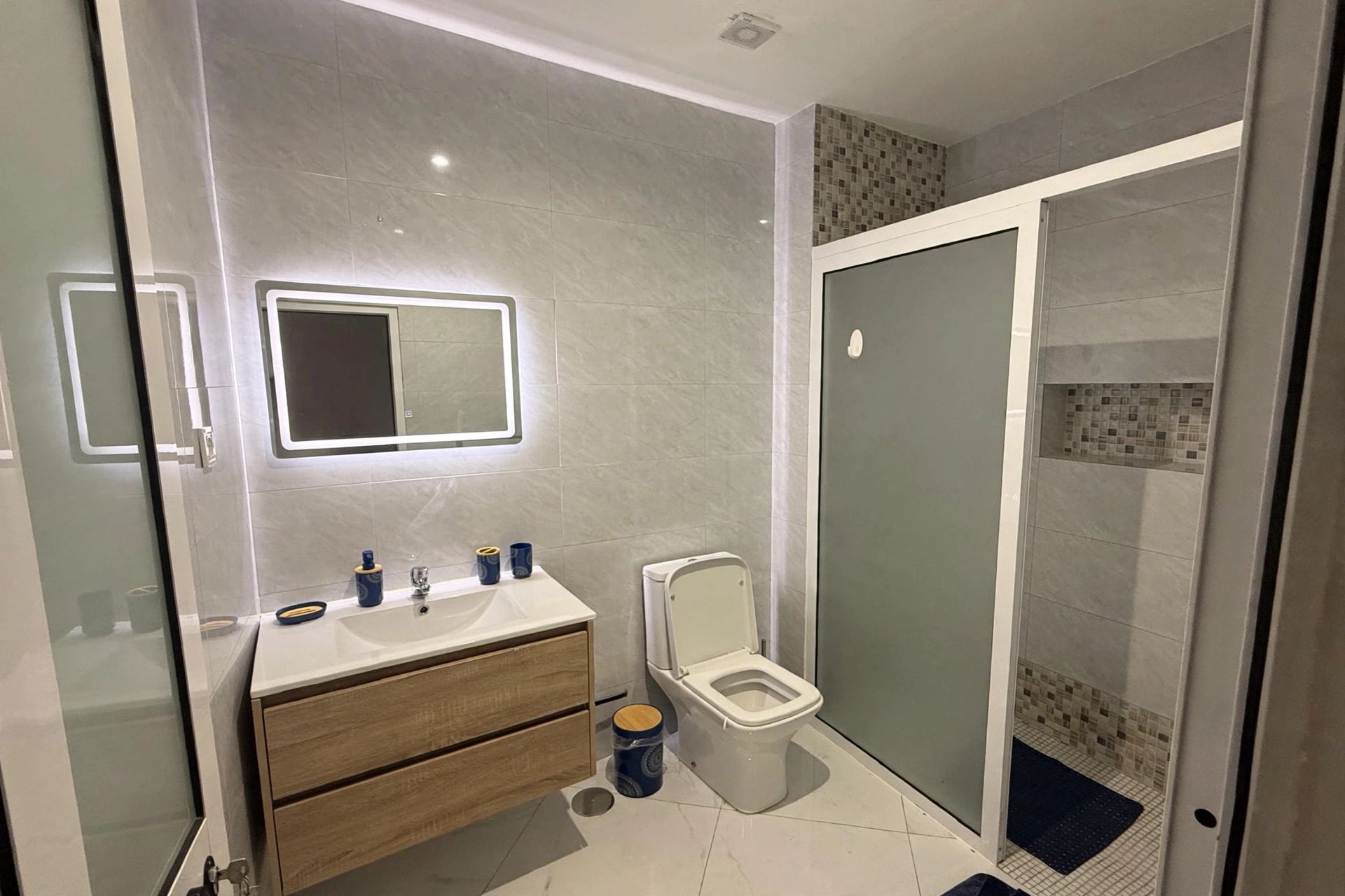 A modern bathroom with a glass shower enclosure, a toilet, and a vanity with a mirror.