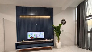 Una sala moderna con un televisor de pantalla plana sobre un soporte de madera, una planta en maceta y un dardo en la pared.