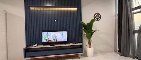 A modern living room with a flat-screen TV on a wooden stand, a potted plant, and a dartboard on the wall.