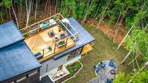 Ein modernes Haus mit einer Holzterrasse, Sitzgelegenheiten im Freien und einem Feuerkorb.