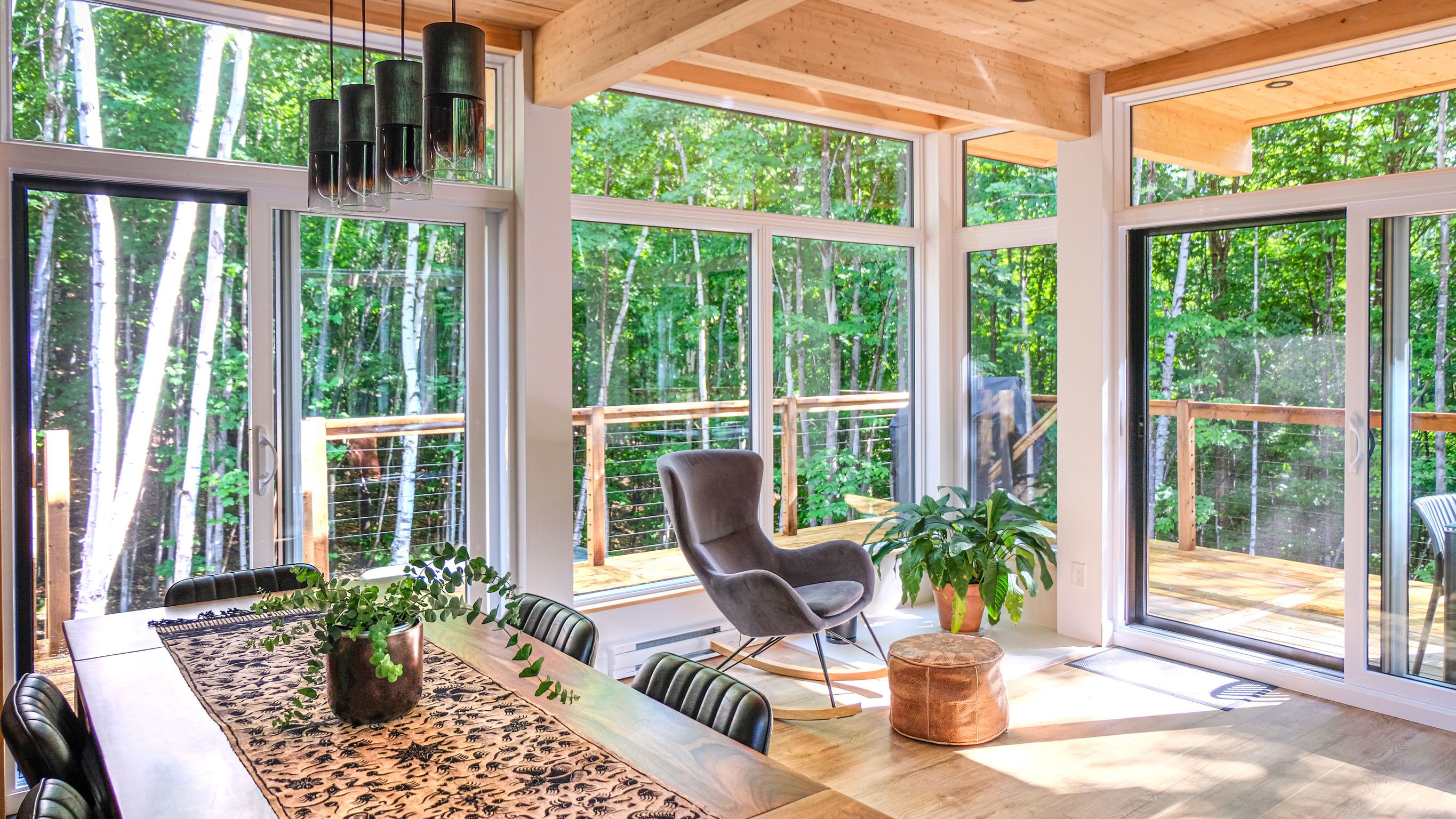 A spacious room with large windows, a dining area, and a seating area with a chair and potted plants.