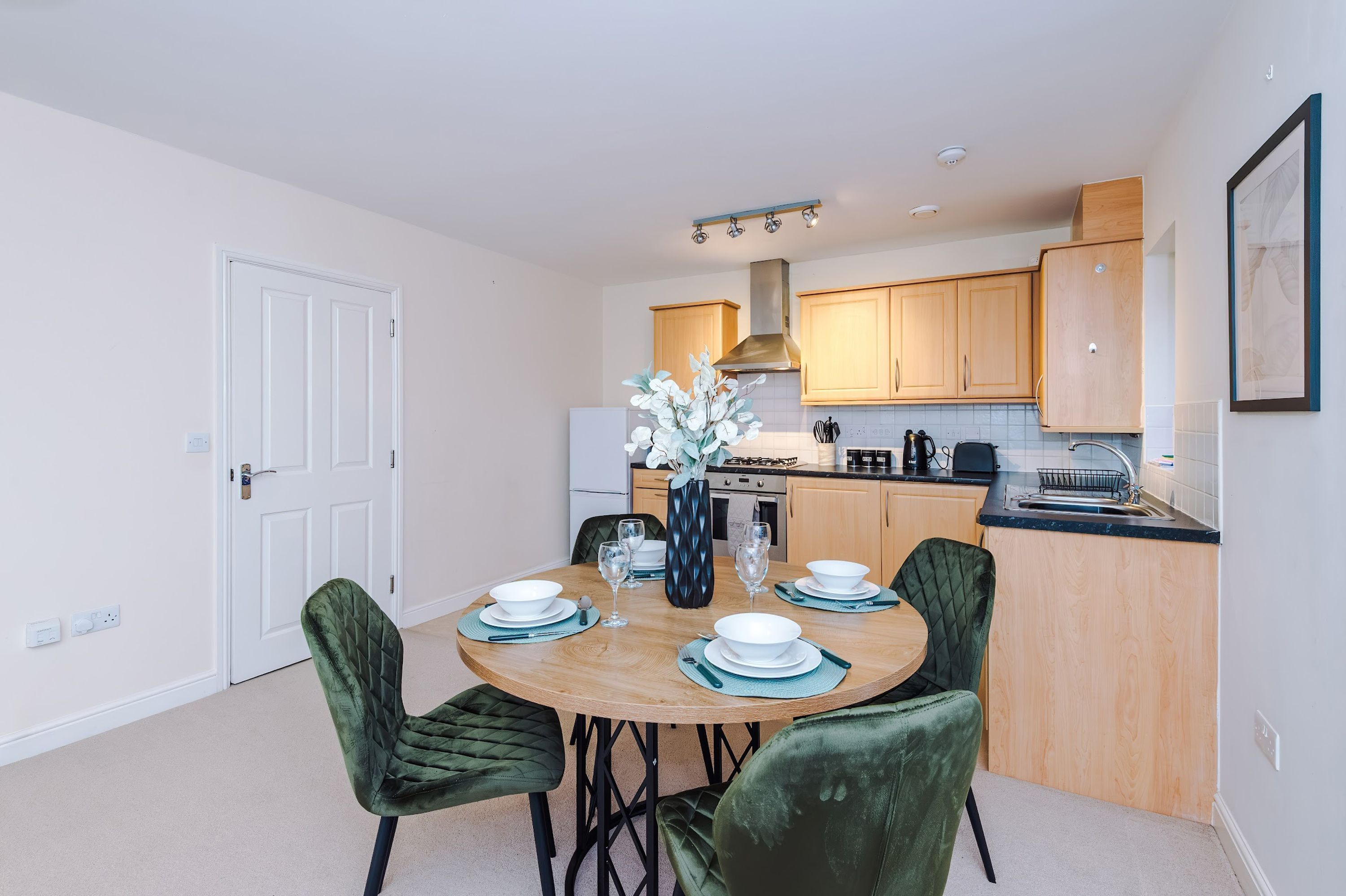 A modern kitchen with wooden cabinets, a gas stove, and a dining area with a round table and green upholstered chairs.