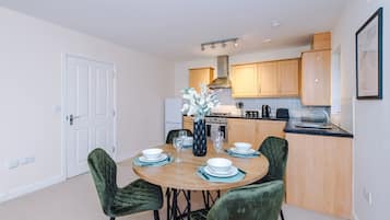 A modern kitchen with wooden cabinets, a gas stove, and a dining area with a round table and green upholstered chairs.