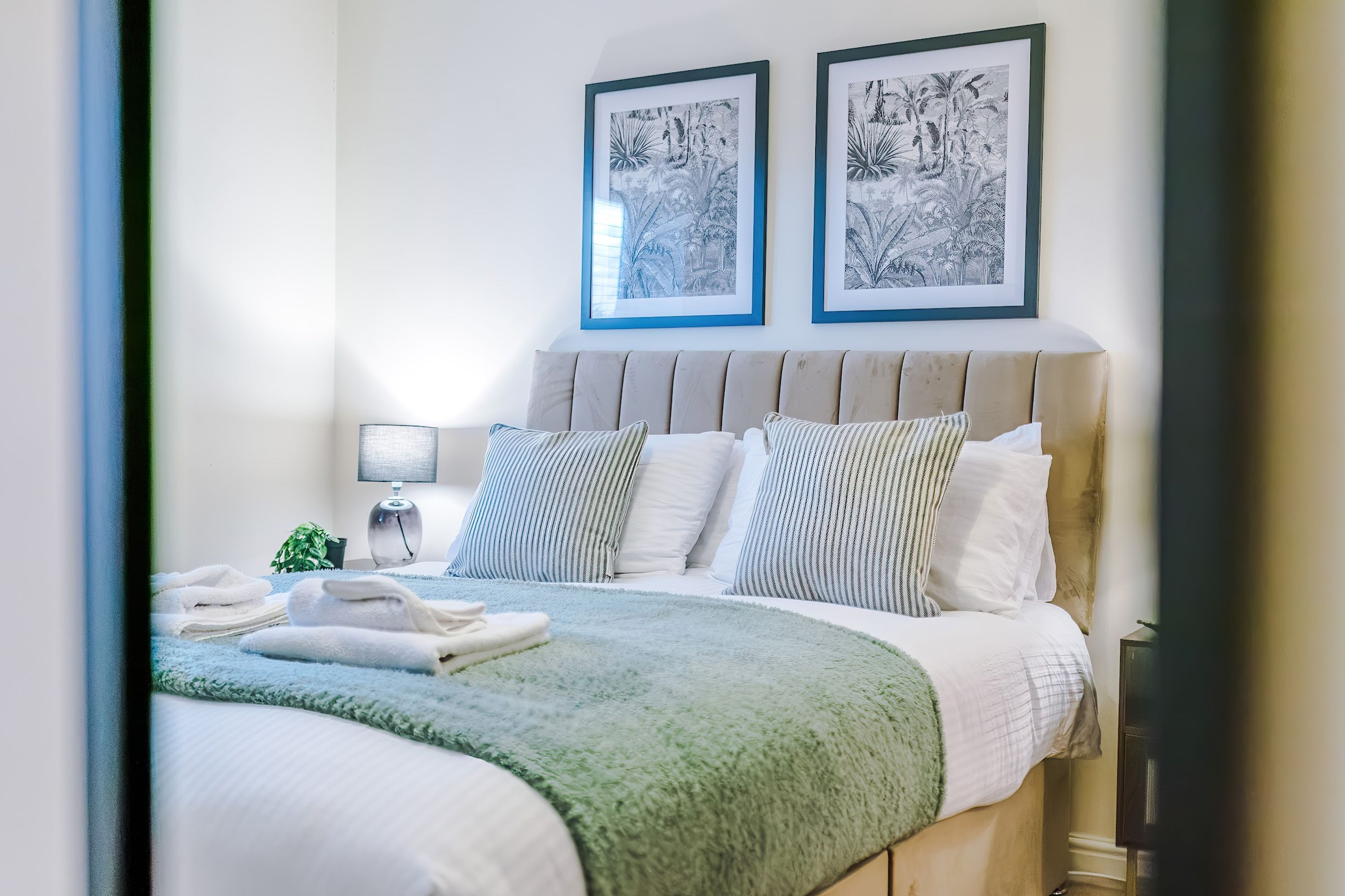 Una cama bien hecha con una manta verde, almohadas blancas y un cabecero con dos cuadros enmarcados.