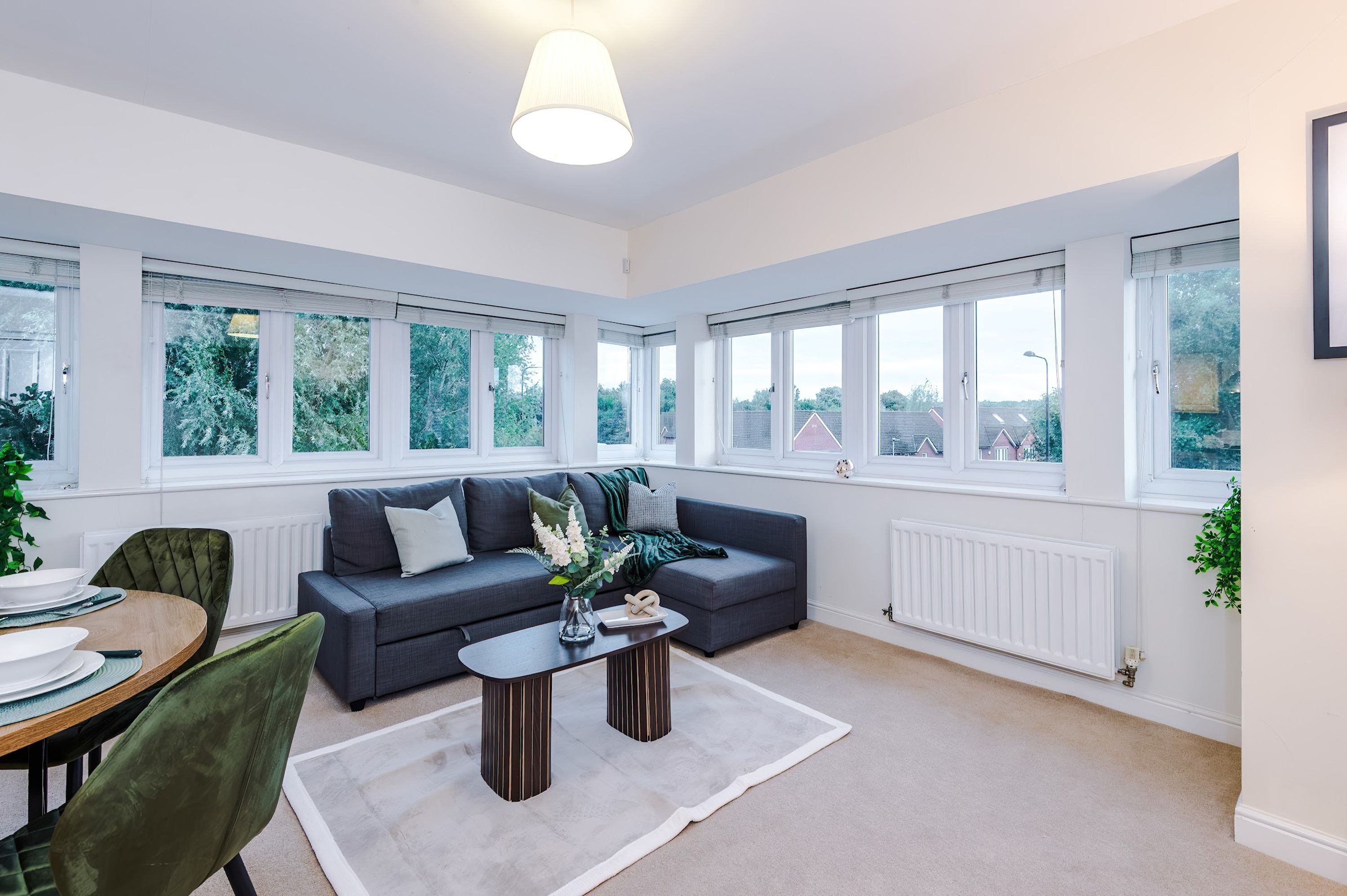 A modern living room with a grey sofa, a coffee table, and a dining area with a table and chairs.