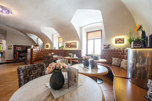 A hotel lobby with round tables, cushioned seating, and a high ceiling with skylights.
