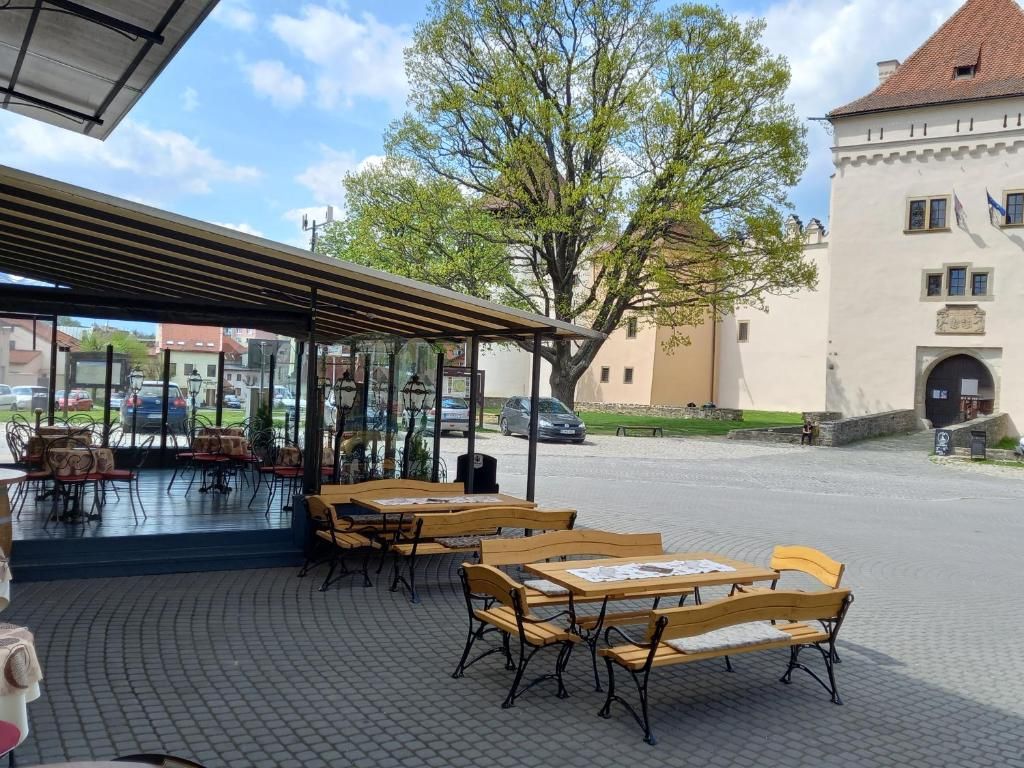 Un espacio al aire libre con mesas y bancos de madera, una zona cubierta con sillas y un árbol grande al fondo.