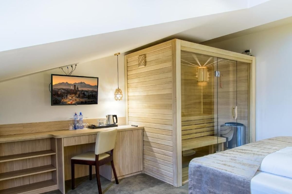 Habitació d'hotel amb escriptori de fusta, una cadira, un llit, zona de dutxa i un quadre al mur.