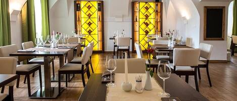 A restaurant with tables set for dining, featuring a modern design with wooden flooring and white chairs.
