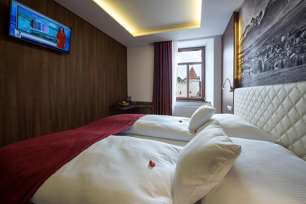 Habitación de hotel con dos camas, un televisor fijado a la pared, una ventana con cortinas y un cuadro colgado en la pared.