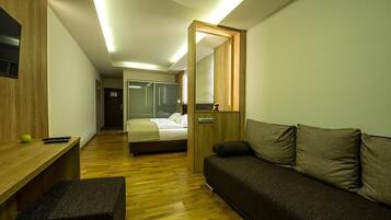 Una camera d'albergo moderna con pavimento in legno, un letto, una poltrona, una scrivania e uno specchio.